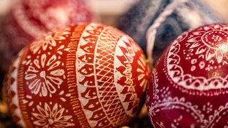 Ein leuchtend rotes Osterei mit weiß eingekratztem Muster. Das Kratzen ist eine beliebte Technik beim Verzieren von Ostereiern.