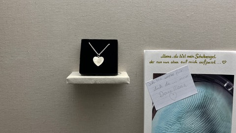 In einem Schaufenster ist eine Kette ausgestellt. Auf ihrem Anhänger erkennt man einen Fingerabdruck. Das ist eine Form der Trauer, die im Museum für Volkskunst ausgestellt ist.