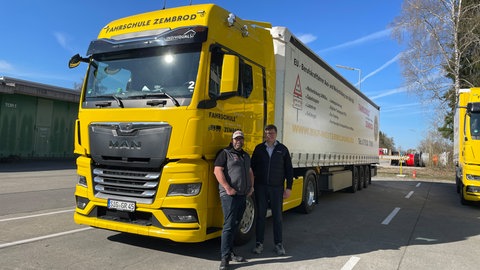 Fahrlehrer Ralph Müller steht mit einem Fahrschüler vom Spritsparkurs vor einem Lkw. Müllers Tipps helfen weniger Kraftstoff zu verbrauchen.