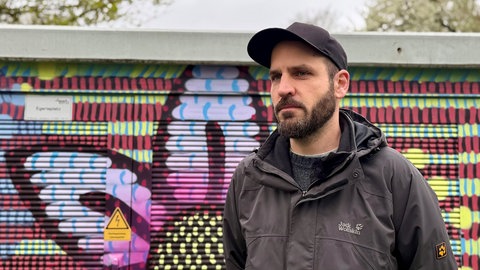 Street Art Künstler Looven steht vor einem selbstgemalten Wandbild. Er malt Auftragsbilder für die Stadtwerke Tübingen. Das wurde durch illegales Graffiti zerstört. 