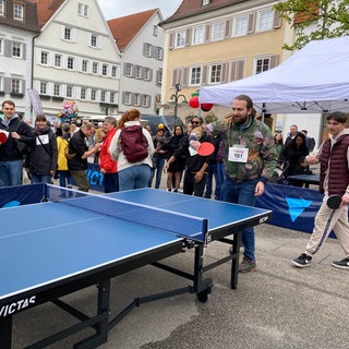 Ein Mann steht an einer Tischtennisplatte und schlägt den Ball über's Netz. Er ist ein Teilnehmer beim Weltrekordversuch im "Mäxle-Tischtennisspiel in Reutlingen.
