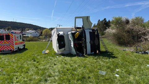 Ein weißer Lastwagen liegt seitlich auf einer Wiese neben einer Bundesstraße. Er ist von der Straße abgekommen und einen Hang hinuntergestürzt.