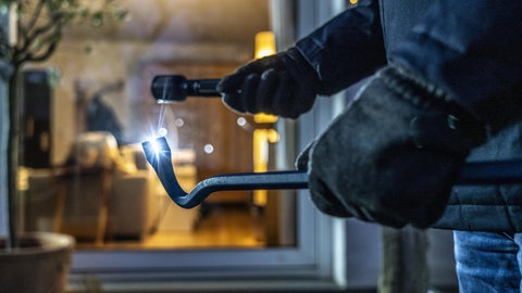 Einbrecher steht mit Brecheisen vor einem Wohnungsfenster. Drei Jugendliche sollen in Wohnung eingebrochen sein. (Symbolfoto)