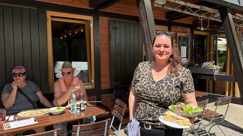 Die Betreiberin Mara-Lisa Odenius steht vor dem Wanderheim "Die Hütte" auf der "Eninger Weide" und hält Kuchen und Salat in den Händen.