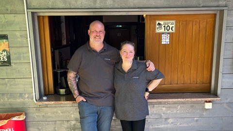 Ein Mann und eine Frau stehen vor einem Kioskfenster. Chris und Jenny Winkler betreiben die Kirchbühlhütte in Mahlstetten.