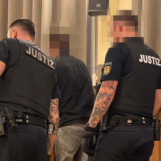 Zwei JVA-Beamte führen den Angeklagten in den Gerichtssaal.