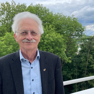 Hintergründig lächelnd lehnt Rammensee am Geländer eines Balkons, hinter ihm Bäume. Hans-Georg Rammensee forscht seit Jahren über das Immunsystem, und wie man es gegen Krebs einsetzen kann. 