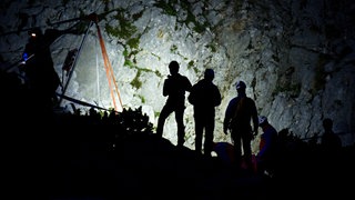 Rettungskräfte der Bergwacht stehen in der Nacht an einem Berg (Symbolbild). Eine Frau aus Baden-Württemberg ist auf die Mondspitze in Vorarlberg gestiegen und saß dann im Dunklen fest.