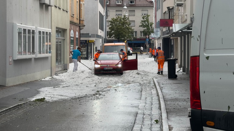 Mitarbeitende der Stadt schippen Hagel nach einem Unwetter in Reutlingen.