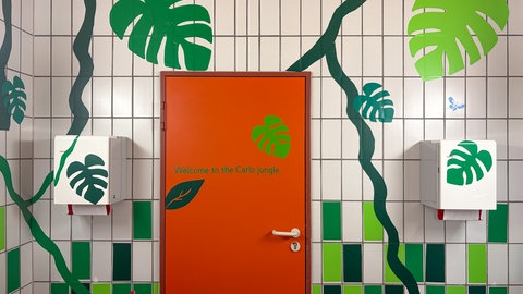 Grüne Blätter und der Schriftzug "Welcome to the Carlo jungle" zieren eine Toilettenwand. Schüler des Carlo-Schmid-Gymnasiums in Tübingen übernehmen die Gestaltung ihrer Schultioletten selbst.