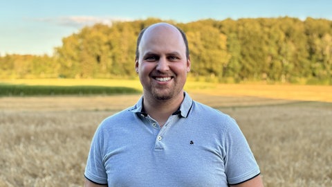 Patrick Schmelcher vom Landwirtschaftsamt Reutlingen steht vor einem Feld. Er findet es wichtig, dass neuartige Technik wie die Aussaat mit Drohnen verbreitet wird.