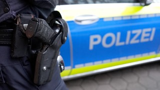 Ein Polizeibeamter steht vor einem Dienstafahrzeug der Polizei. 