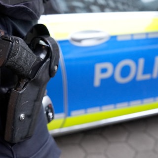 Ein Polizeibeamter steht vor einem Dienstafahrzeug der Polizei. 