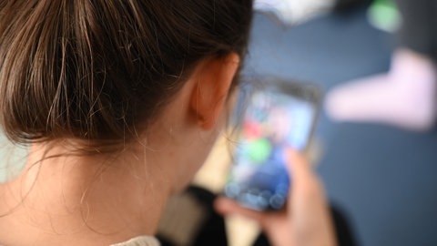 Blick über die Schulter: Eine 18-jährige Frau schaut gebannt auf ihr Handy