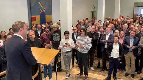 Oberbürgermeister Martin Ansbacher steht vor den Menschen im Foyer des Ulmer Rathauses. 