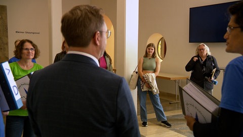Emilia Stella Schneider steht in einem Kreis mit mehreren Menschen im Rathaus, während der Ulmer Oberbürgermeister Martin Ansbacher in die Runde spricht. Emilia wird eine der jüngsten Stadträte in Baden-Württemberg. Ihr politisches Interesse wurde vor allem durch das Projekt "Jugendaktiv in Ulm" geweckt. 