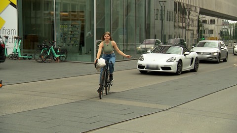 Emilia fährt auf dem Fahrrad, hat einen Arm ausgestreckt um anzuzeigen, dass sie links abbiegt. Sie fährt Richtugn Ulmer Rathaus. Emilia ist in der Regel mit dem Fahrrad unterwegs. Bessere Radinfrastruktur ist auch eines ihrer Anliegen für den Gemeinderat.