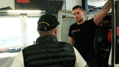 Enrico Hiller lehnt sich an den Kofferraum seines Firmenautos und blickt mit ernstem Gesicht zu einem Kunden. Der steht mit dem Rücken zur Kamera, da er nicht erkannt werden will. Er ist Opfer von Betrügern geworden und an eine unseriöse Reinigungsfirma geraten, die seine Notlage ausgenutzt haben und 1.700 Euro für eine "Nichtleistung" verlangten. 