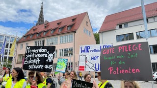 Pflegekräfte halten Plakate mit Forderungen für bessere Arbeitsbedingungen und mehr Lohn in die Höhe. Beschäftigte an der Uniklinik Ulm streiken für mehr Lohn und bessere Arbeitsbedingungen.