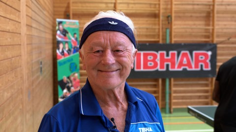 Hans Ohlhauser lächelt in die Kamera. Auf der Stirn sein Markenzeichen: Das Stirnband. Er tritt bei der Senioren WM im Tischtennis in Rom an.
