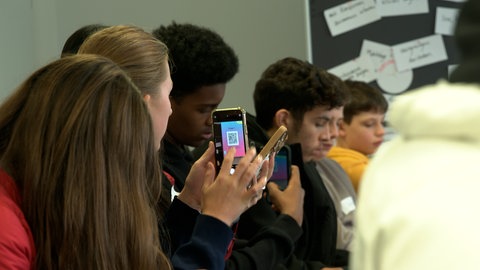 Schülerinnen und Schüler zücken beim Newscamp von SWR und SWP in Ulm ihr Handy bei einem interaktiven Workshop zum Thema Influencer und Desinformation.