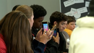 Schülerinnen und Schüler zücken beim Newscamp von SWR und SWP in Ulm ihr Handy bei einem interaktiven Workshop zum Thema Influencer und Desinformation.