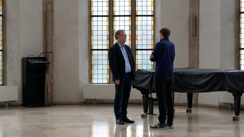 Dekan Torsten Krannich steht mitten in einem großen, kirchlichen Gebäude und ist im Gespräch mit einem SWR-Reporter. Er befasst sich mit dem Psychoterror in Langenau und steht im Kontakt mit Pfarrer Ralf Sedlak.