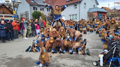 Umgeben von Zuschauerinnen und Zuschauern bilden die in ein blau-braunes Häs gehüllten Donau-Ratzen mit ihrer rattenartigen Holzmaske eine Pyramide.
