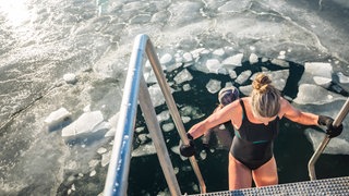 Ganz langsam, Stufe für Stufe, geht eine Frau eine Treppe zum Eisbaden hinunter. Eisbaden liegt im Trend: Sobald die Temperaturen wieder sinken, begeben sich viele Menschen in den See, Fluss oder in die Eistonne.