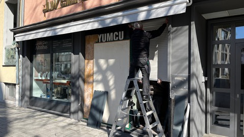 Handwerker ersetzen die zerstörte Jalousie am Juweliergeschäft. Zwei Männer sind am Sonntagmorgen mit einem gestohlenen Transporter in das Schaufenster eines Ulmer Juweliers gefahren. Die Polizei geht von einem gescheiterten Einbruchsversuch aus.