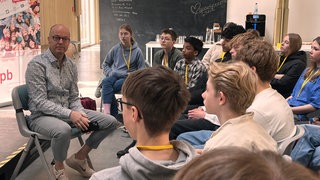 Jugendliche sitzen im Halbkreis um einen Mann herum. Beim Newscamp in Schwäbisch Gmünd sensibilisiert SWR-Reporter Jürgen Klotz die Jugendlichen auch in Sachen Fake-News.