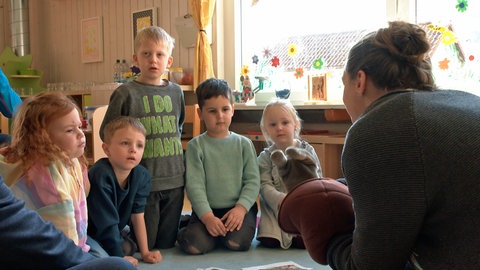 Svenja Posiadlo sitzt fünf Kindern gegenüber. Sie hat sich eine Handpuppe übergestülpt. Sie ist eine von rund 1.700 Quereinsteigern in Kitas, ausgebildet durch ein Programm des Landes Baden-Württemberg, um Personalmangel entgegenzuwirken.