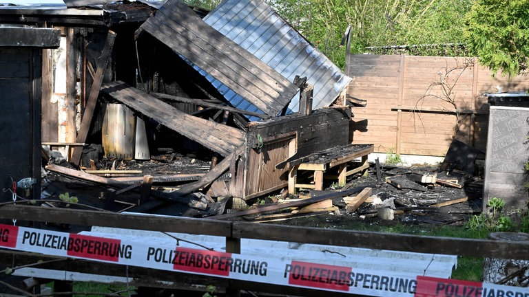 Absperrband vor einer zerstörten Gartenhütte. Das Dach der Hütte ist beim Brand in der Kleingartenanlage in Langenau eingestürtzt. 