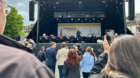 Mehrere Besucher machen Fotos oder filmen die Eröffnung des Deutschen Musikfestes in Ulm und Neu-Ulm auf dem Münsterplatz.