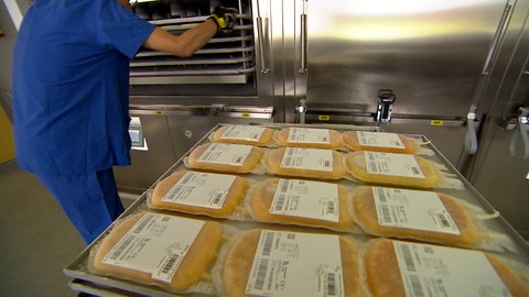 Eine Mitarbeiterin schiebt Bleche mit Blutplasmabeuteln in einen Tiefkühler.