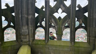 Ein Seil hängt außen am Turm des Ulmer Münsters, ein Mann mit Helm - ein Industriekletterer - ist dort abgeseilt und inspiziert die Außenfassade auf mögliche lose Teile.