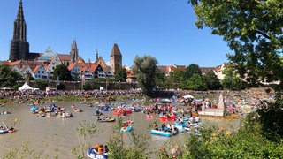Viele Nabader und Boote auf der Donau, im Hintergrund das Münster und mehrere Türme, die das Stadtbild prägen.