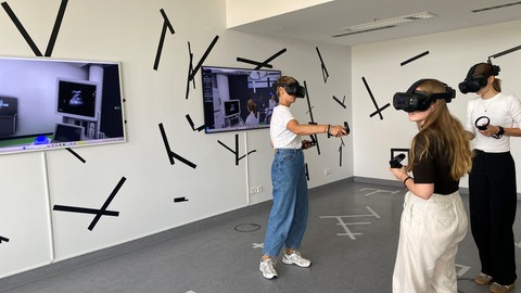 Medizinstudentinnen und Studenten üben in einem Virtuellem Schockraum in der Universität Ulm. Carmen Maier (ganz links) macht die Anästhäsie, während Jutta Karmann (Mitte) sich mit Ultraschall den Patienten untersucht. Auf dem linken Bildschirm ist das echte Ultraschallbild des verunfallten Motorradfahrers zu sehen. Marie Mücke (rechts) kümmert sich ebenfalls um den Patienten.