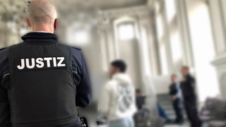 Ein Justizbeamter steht im Gerichtssaal, in dem gegen drei Brüder aus Aalen verhandelt wird. Die drei Angeklagten sollen einen Mann entführt und erpresst haben. Ein Urteil vor dem Landgericht Ellwangen soll am Mittwoch fallen.