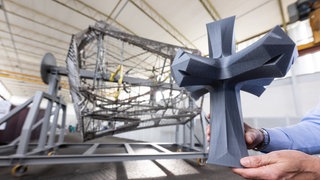 Ein Modell der Kirchturmspitze der Sagrada Família ist in einer Halle vor einem Bauteil des Kreuzes zu sehen. Mit ihm soll das Ulmer Münster beim Rekord des höchsten Kirchturms der Welt abgelöst werden.