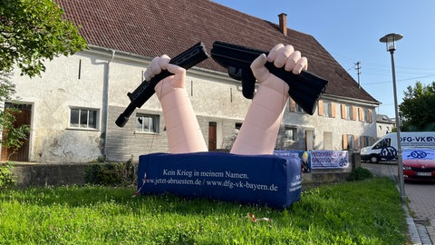 Vor einem Haus auf einer Wiese ist ein Luftkissen in Form vor zwei Händen mit einer durchgebrochenen Waffe zu sehen. Friedensaktivisten und -akivistinnen hatten in Kellmünz gegen ein Kinderferienprogramm der Bundeswehr protestiert.
