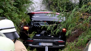 Ein Auto steht demoliert in einer Hecke: In seinem eigenen Garten wurde ein 60-Jähriger zum Unfallopfer, als der Fahrer des schwarzen Wagens plötzlich durch die Hecke brach.