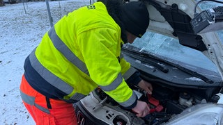 Marcel Selke ist bei der Arbeit und startet ein Auto mit Hilfe eines Überbrückungskastens. 