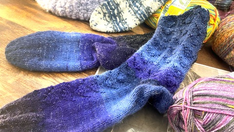 Blaue Socken neben bunten Wollknäulen - bei der Strick-Aktion werden vor allem Socken in größeren Größen gestrickt, damit sie flexibel eingesetzt werden können. 
