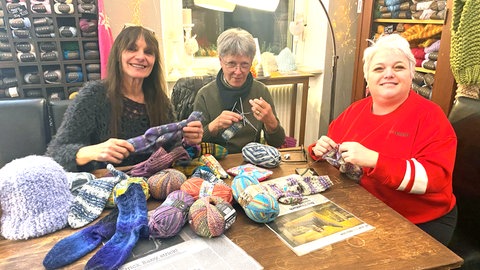 Frauen am Tisch mit einem Haufen Wolle - sie stricken für Obdachlose gemeinsam Socken.