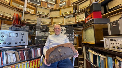 Werner Hauf in seinem Museum für Radios: 1.300 historische Geräte hat er mittlerweile gesammelt. Das Radio auf seinem Schoß ist sein erstes in der Sammlung, ein Lomophon Gloria 33.