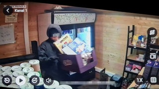 Ein Vermummter stiehlt in einem Laden Lebensmittel. Aufgenommen wurde das Bild von einer Überwachungskamera eines Selbstbedienungsladens.