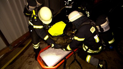 Feuerwehrleute legen eine Patientien auf eine Trage und transportieren sie ab.