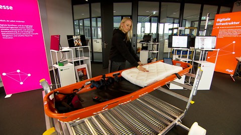 Eine Frau steht an einer Rettungstrage und drückt mit der flachen Hand auf eine Matraze. Die Sensoren in der Matraze übertragen die Daten auf ein Tablett.