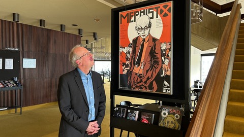 Intendant des Theaters Ulm, Kay Metzger steht neben dem Plakat des neuen Stücks "Mephisto" dass durchaus Parallelen zur Geschichte von Herbert von Karajan hat. 